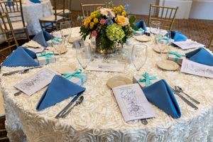 Elegant wedding reception tables with blue napkins and floral centerpieces on white textured linens.