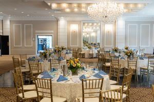 Elegant banquet hall with crystal chandeliers, gold chiavari chairs, and white wainscoting features luxurious wedding reception setup.
