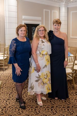 Four women in navy blue and floral dresses pose on an elegant carpeted floor with gold chairs in the background.