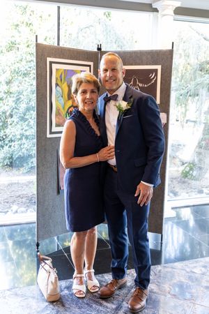 A couple dressed in formal attire poses together at an event, with artwork visible in the background.