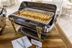Taquitos or rolled tacos lined up neatly in a stainless steel chafing dish on a wooden table.