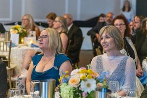Guests seated at round tables with yellow floral centerpieces during an indoor celebration.