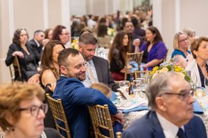 Rows of guests seated at banquet tables during a formal indoor celebration event.
