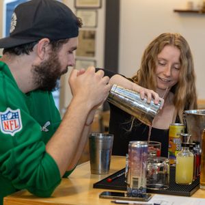 People in green hoodies sit at table sharing drinks and snacks during casual gathering.