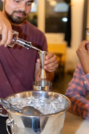 Group of people around a table preparing cocktails with ice and mixing tools in a bar setting.