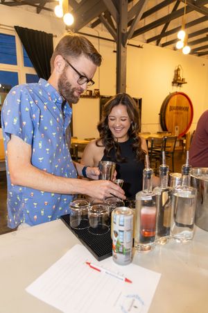 People participating in a cocktail making workshop at a wooden table in an industrial style space.