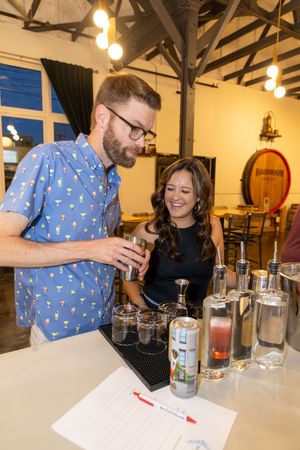 People gathered around a table for a wine tasting event with several glasses displayed in a rustic indoor setting.
