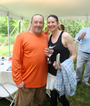 Two people share a moment under a white outdoor tent at a casual gathering in nature.