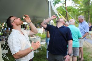 People at an outdoor celebration event hold up beverages while gathering in a garden party setting.