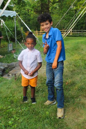 Two young friends pose together on grass near party tents at an outdoor event.