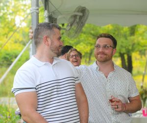 Three people enjoying conversation and laughter together outdoors on a sunny day amid green foliage.