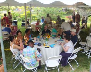 Outdoor gathering with people seated at tables under a tent canopy with mountains in the background.