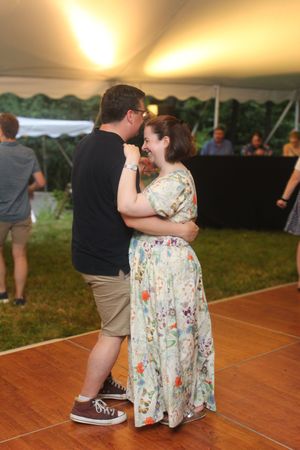 A couple shares an intimate dance moment under party tent lighting at dusk.