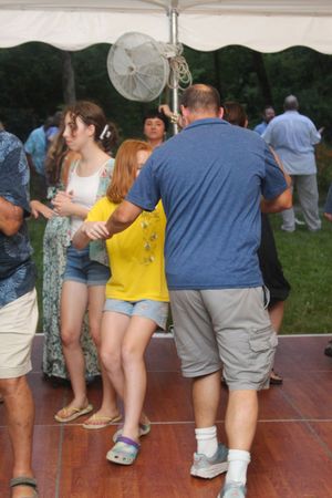 People in casual attire dancing in a line at an outdoor party on a wooden deck.