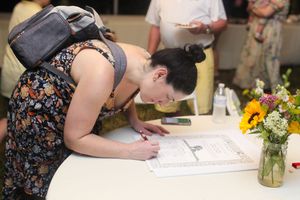 Multiple people signing a guestbook at a table decorated with floral centerpieces.