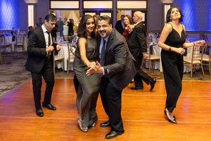 Couples dancing elegantly at a formal gala event in a ballroom with white tablecloths and warm lighting.