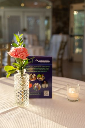 Elegant table setting with pink carnation in crystal vase, purple event program and glowing tea light candle.