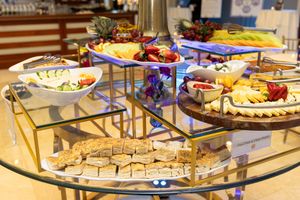 Elegant multi-tiered glass buffet display with fresh fruits, sandwiches, and colorful appetizers at a catered event.