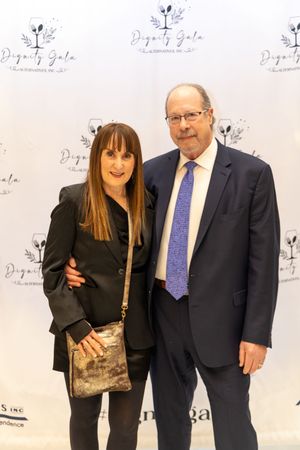 Couple posing together at the Dignity Gala event, dressed in formal attire against a branded backdrop.