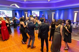 A large ballroom with blue ambient lighting and people spread across the dance floor during an event.