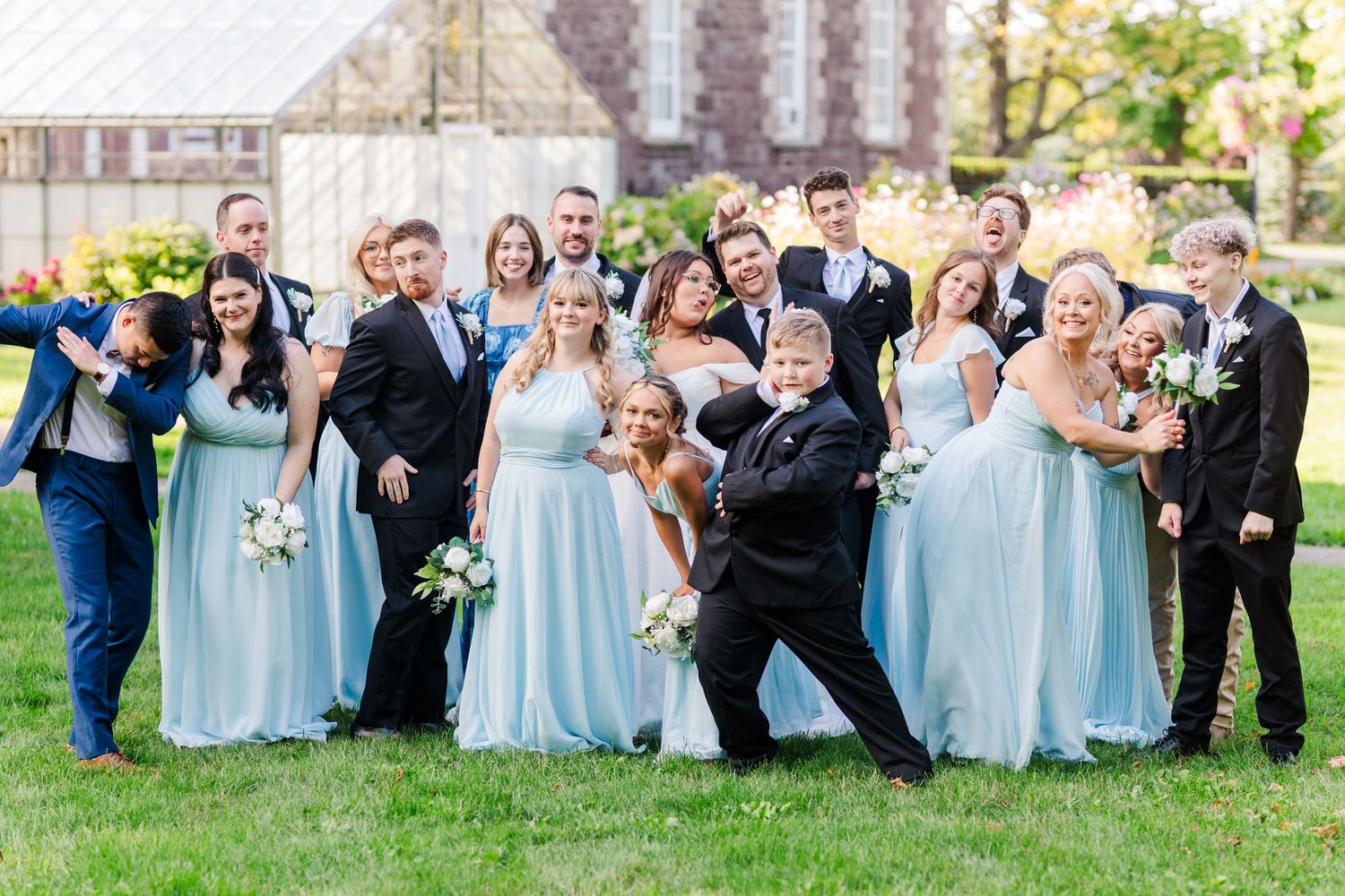 Wedding party wearing light blue and navy poses playfully in sequence at outdoor garden ceremony celebration.