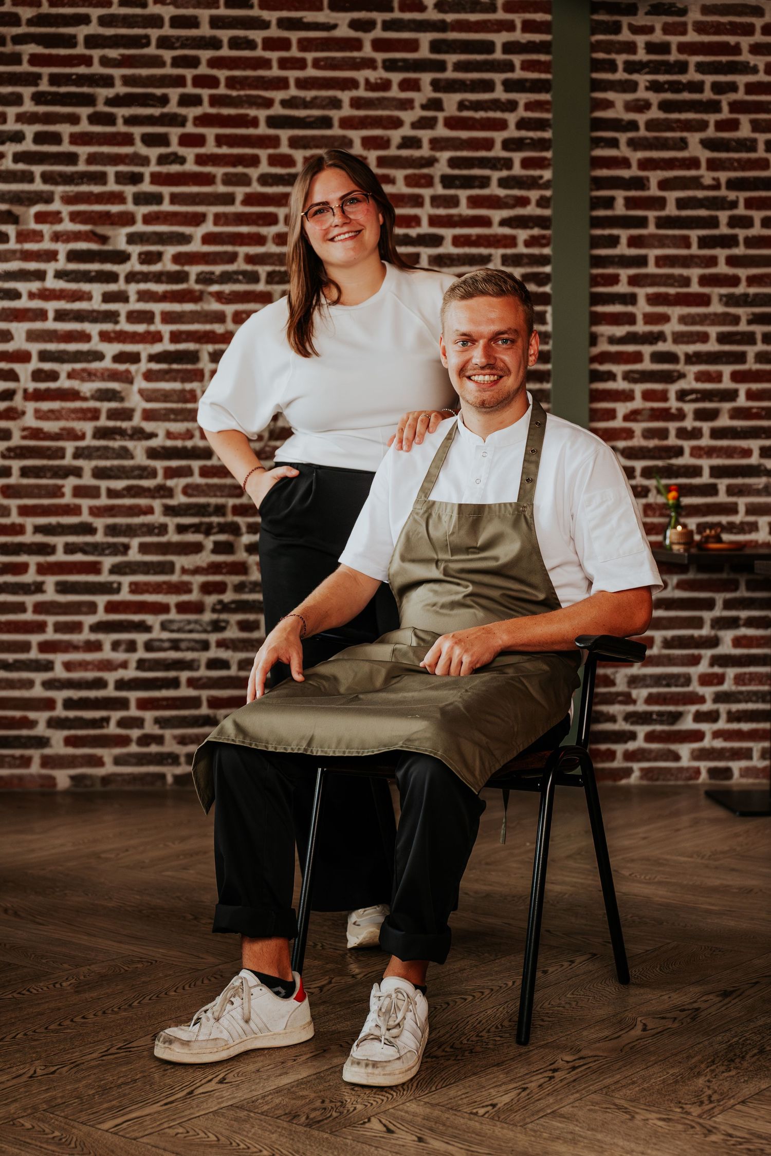 A casual indoor portrait session featuring someone seated in a chair against a rustic brick wall background.