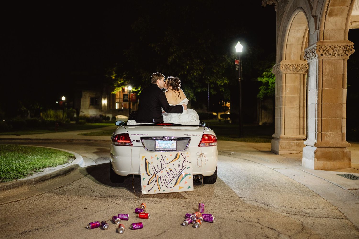 Nighttime view of a car parked in front of architectural columns with pink lights and scattered items on ground.