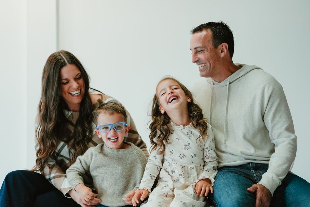 Happy family laughing together on white couch in matching sweaters.