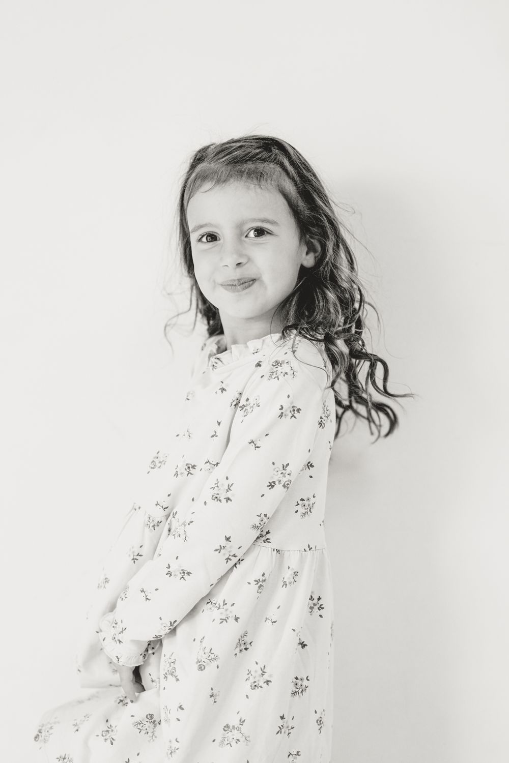 Child in floral dress posing against white background in minimalist portrait series.