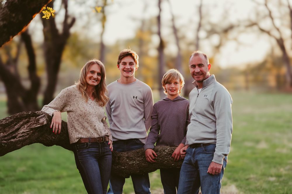 Family of four sitting casually together on fallen tree trunk in outdoor setting.