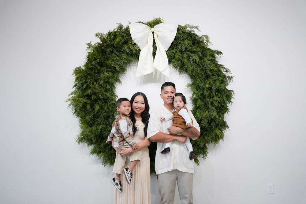 Family portrait session with a large decorative Christmas wreath against white backdrop.
