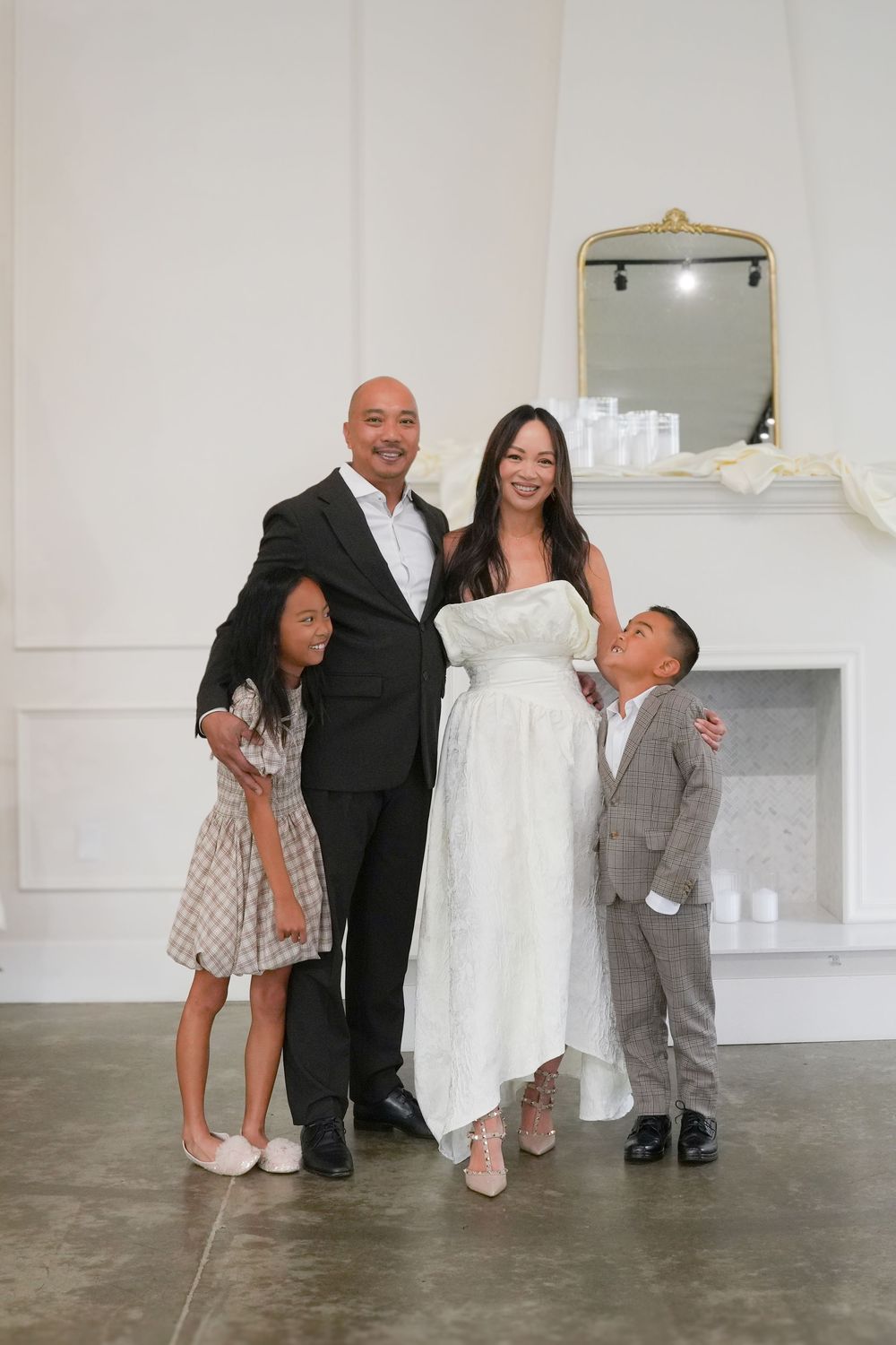 Indoor photoshoot with a white dress display and family members in formal attire.