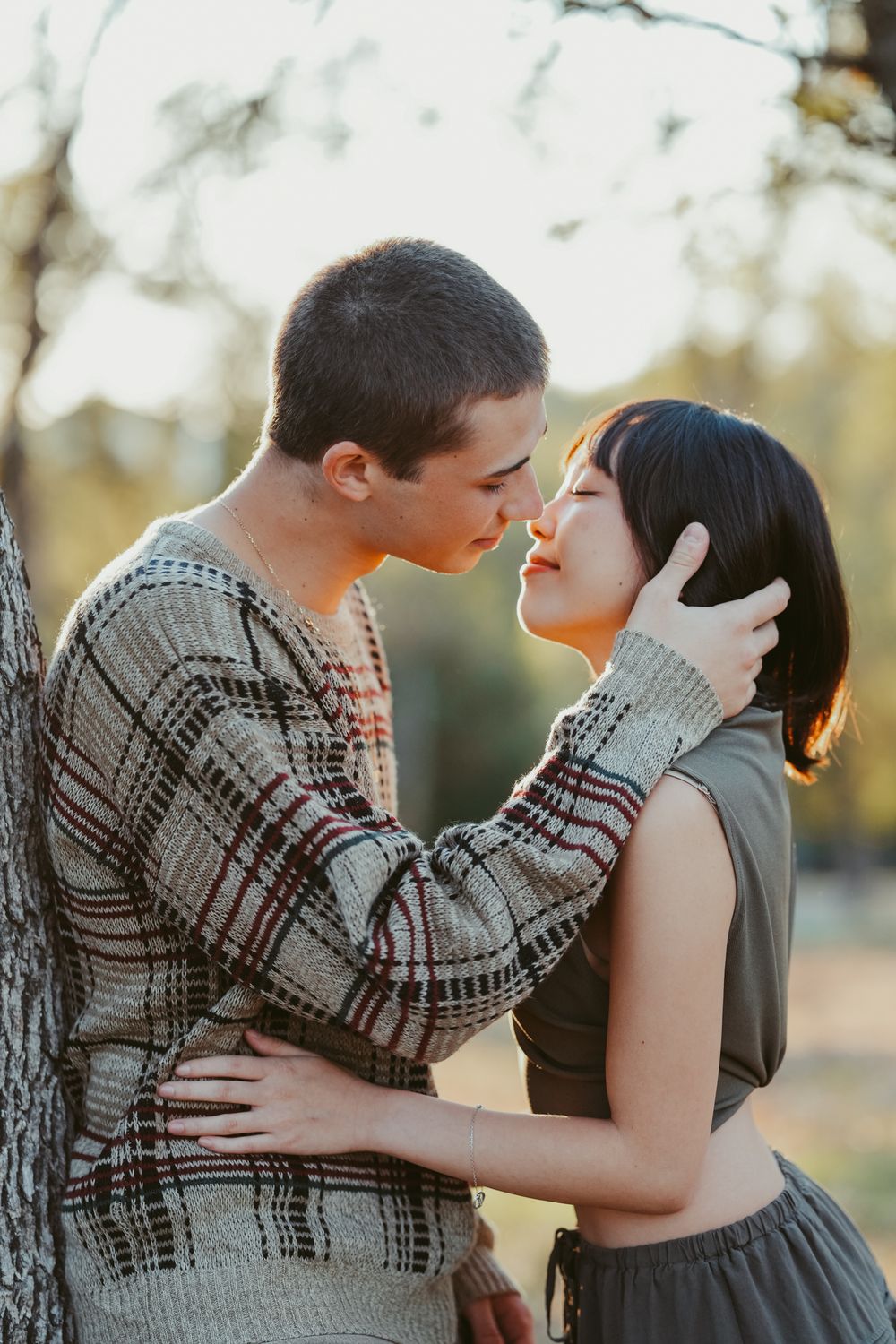 Romantic couple in casual attire embracing near trees at sunset.