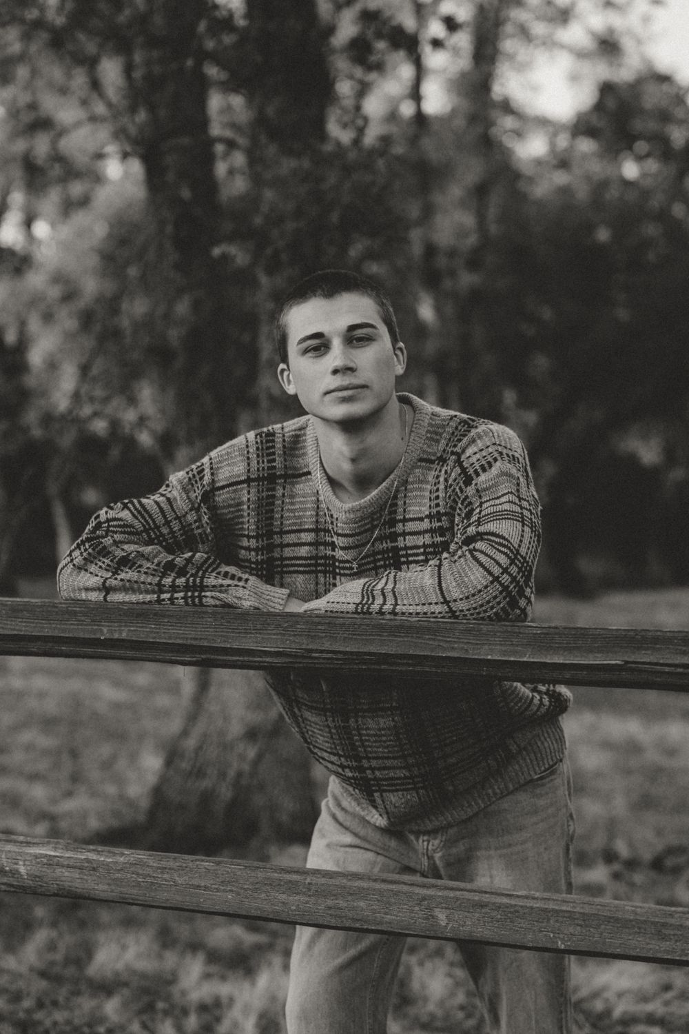 Person in plaid shirt leaning on wooden fence in black and white portrait.