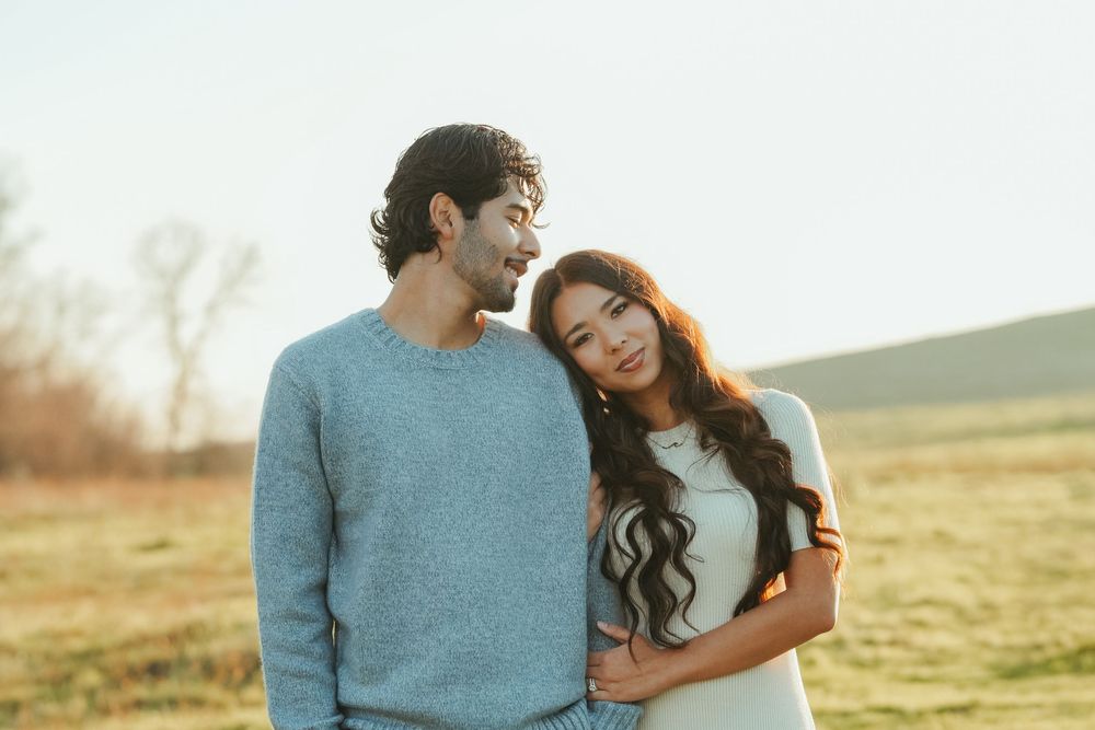 Couple sharing an intimate moment in golden sunlight on grassy hillside.