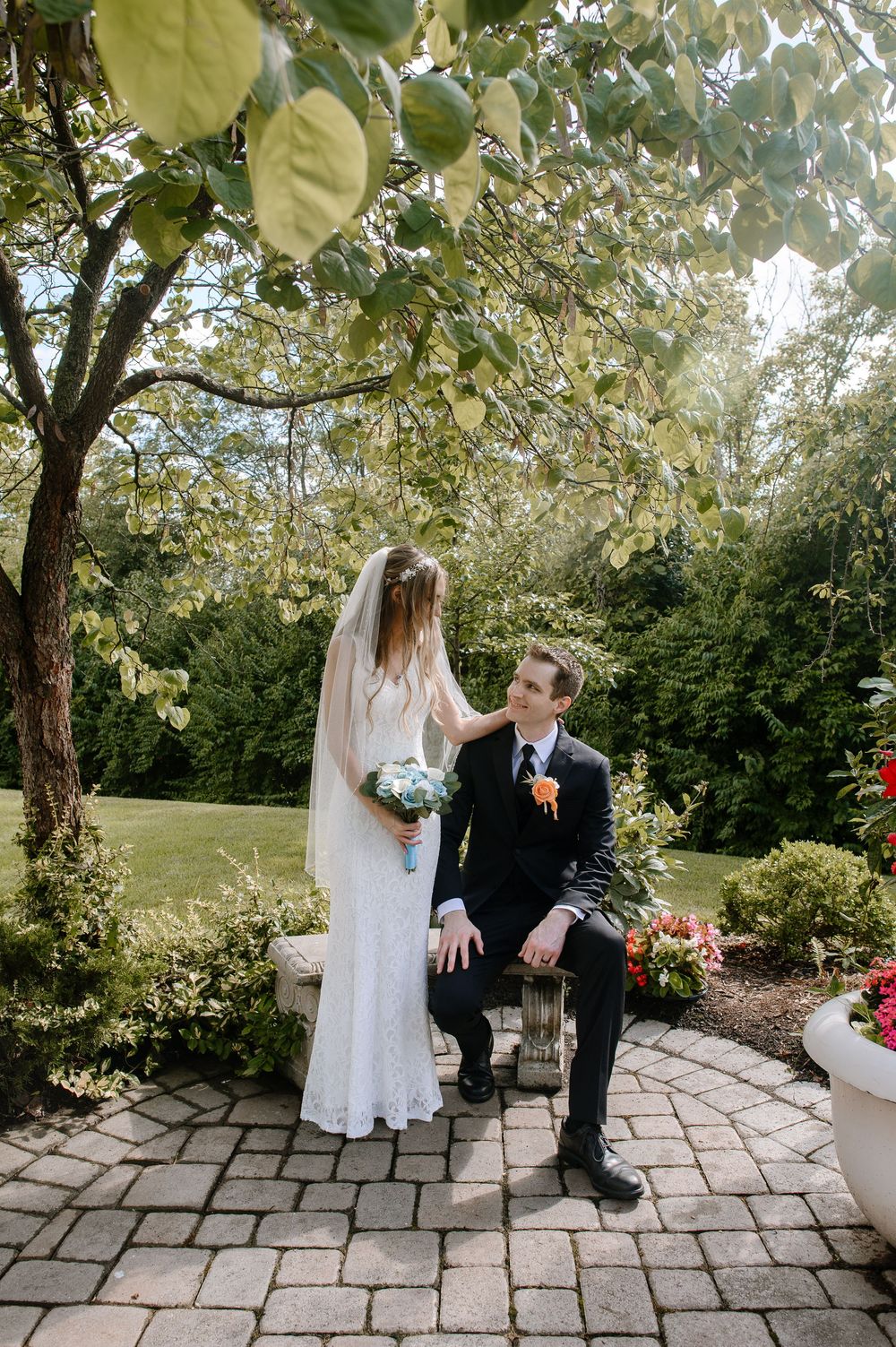 Wedding couple shares a moment in a sunlit garden with blooming trees and stone patio.