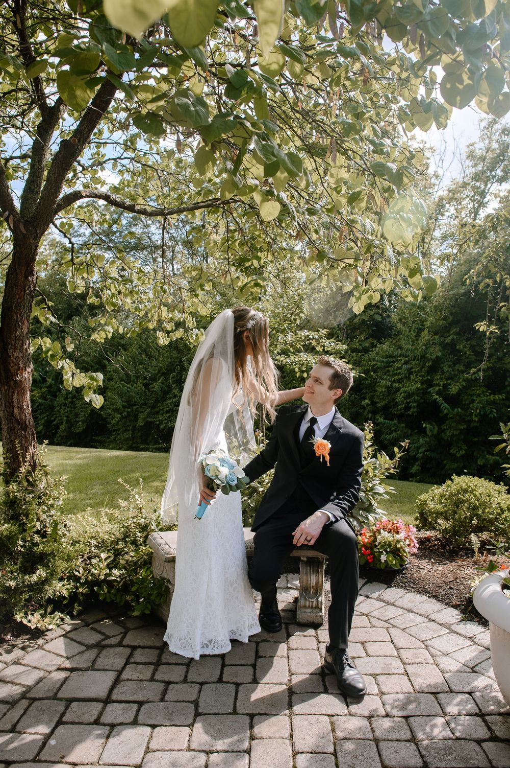 Romantic outdoor wedding photos being taken on a paved garden path surrounded by trees and sunlight.