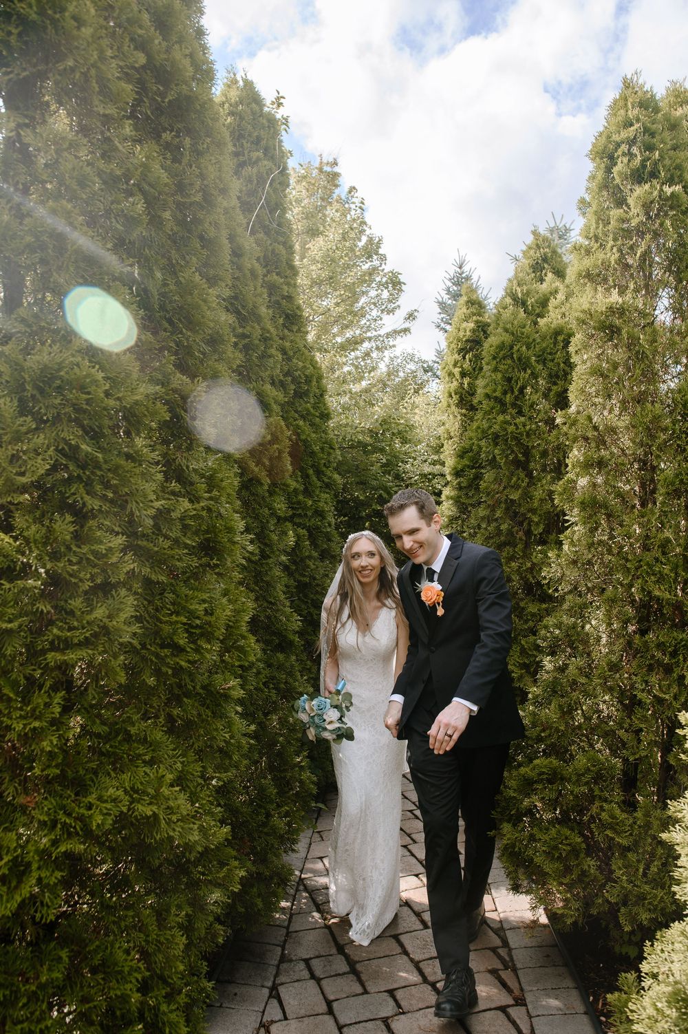 Wedding couple shares intimate moments on a stone pathway surrounded by tall evergreen trees.