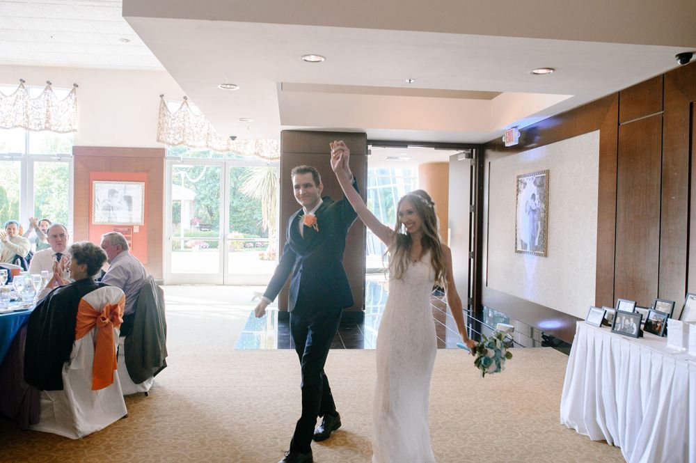 Wedding celebration in a bright reception hall with guests seated at decorated tables.