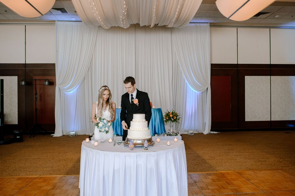 Couple sits at elegant white-draped reception table during wedding celebration in banquet hall.