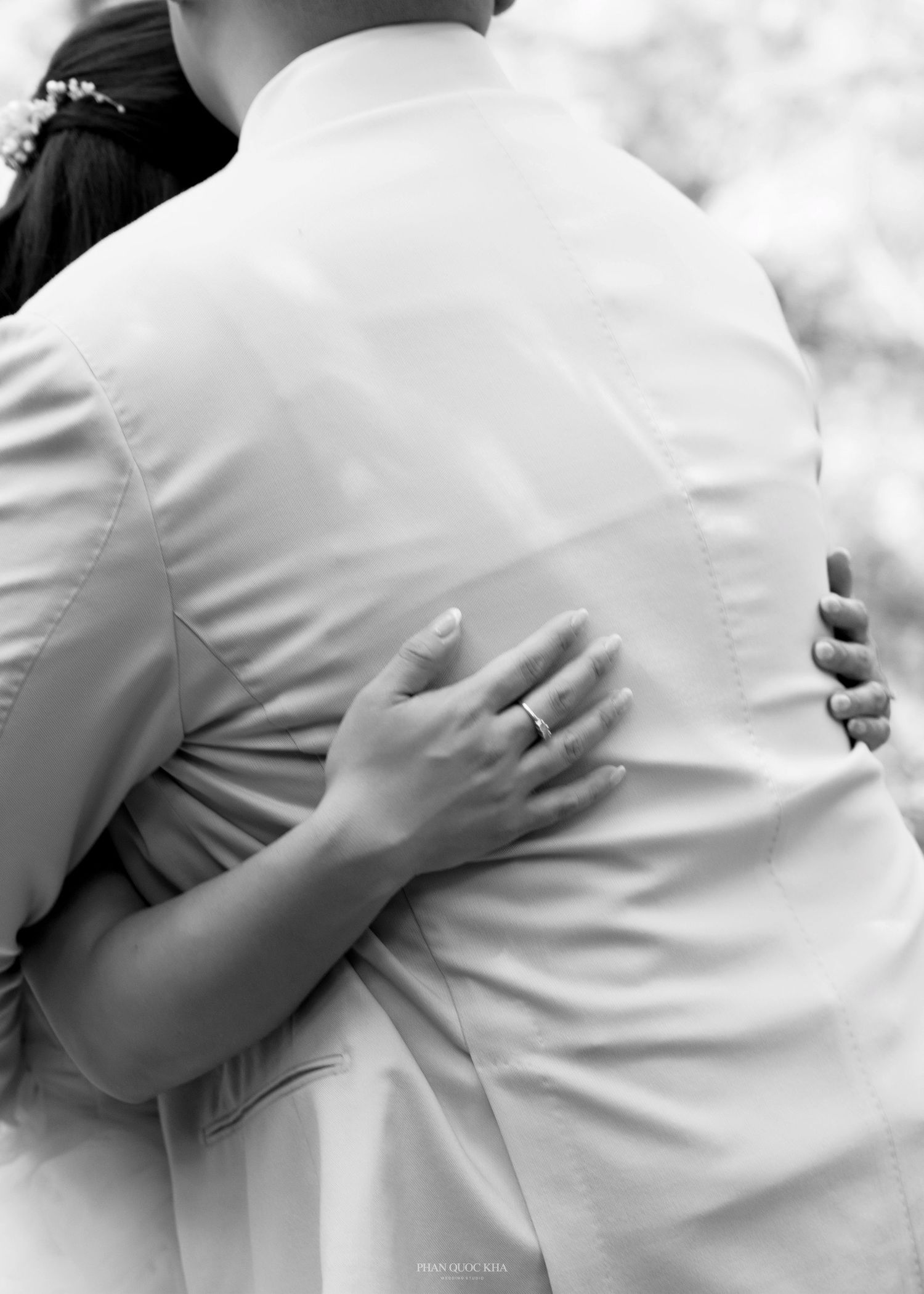 Black and white close-up of bride's hand with ring embracing groom's back.