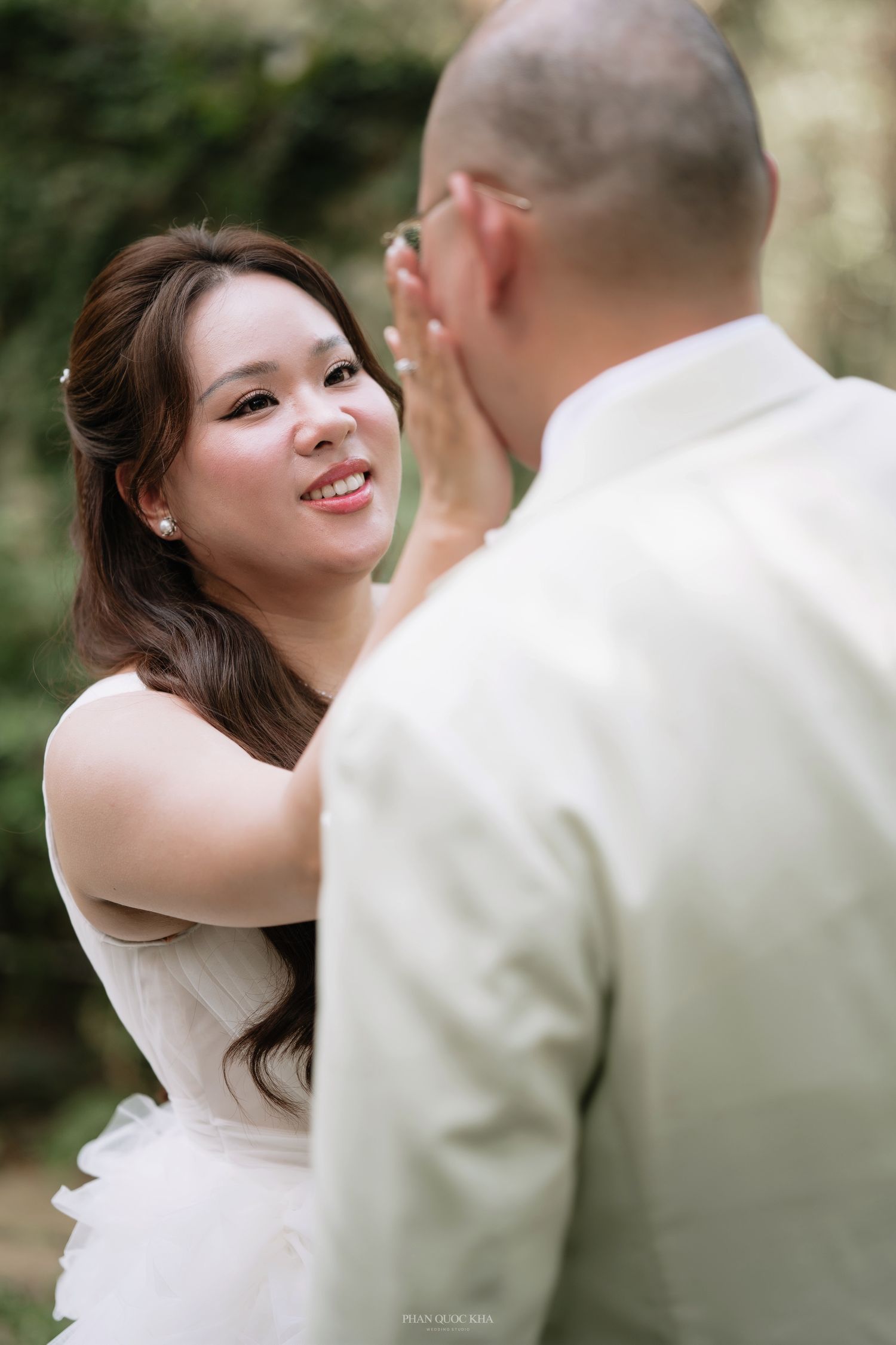 Emotional bride in white tulle gown tenderly touching grooms face during outdoor first look moment.