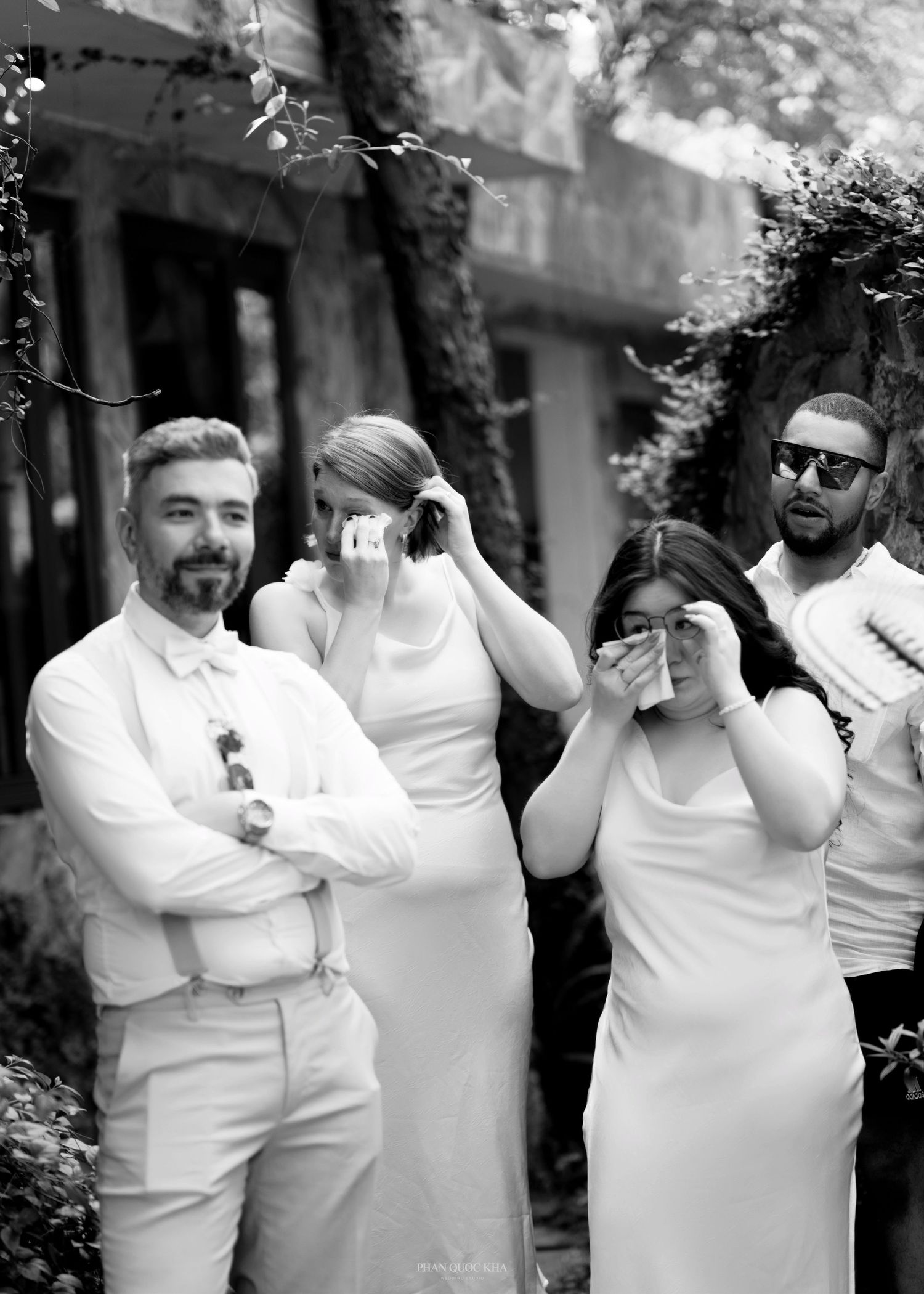 Black and white photo of wedding guests wiping tears during an emotional outdoor ceremony.