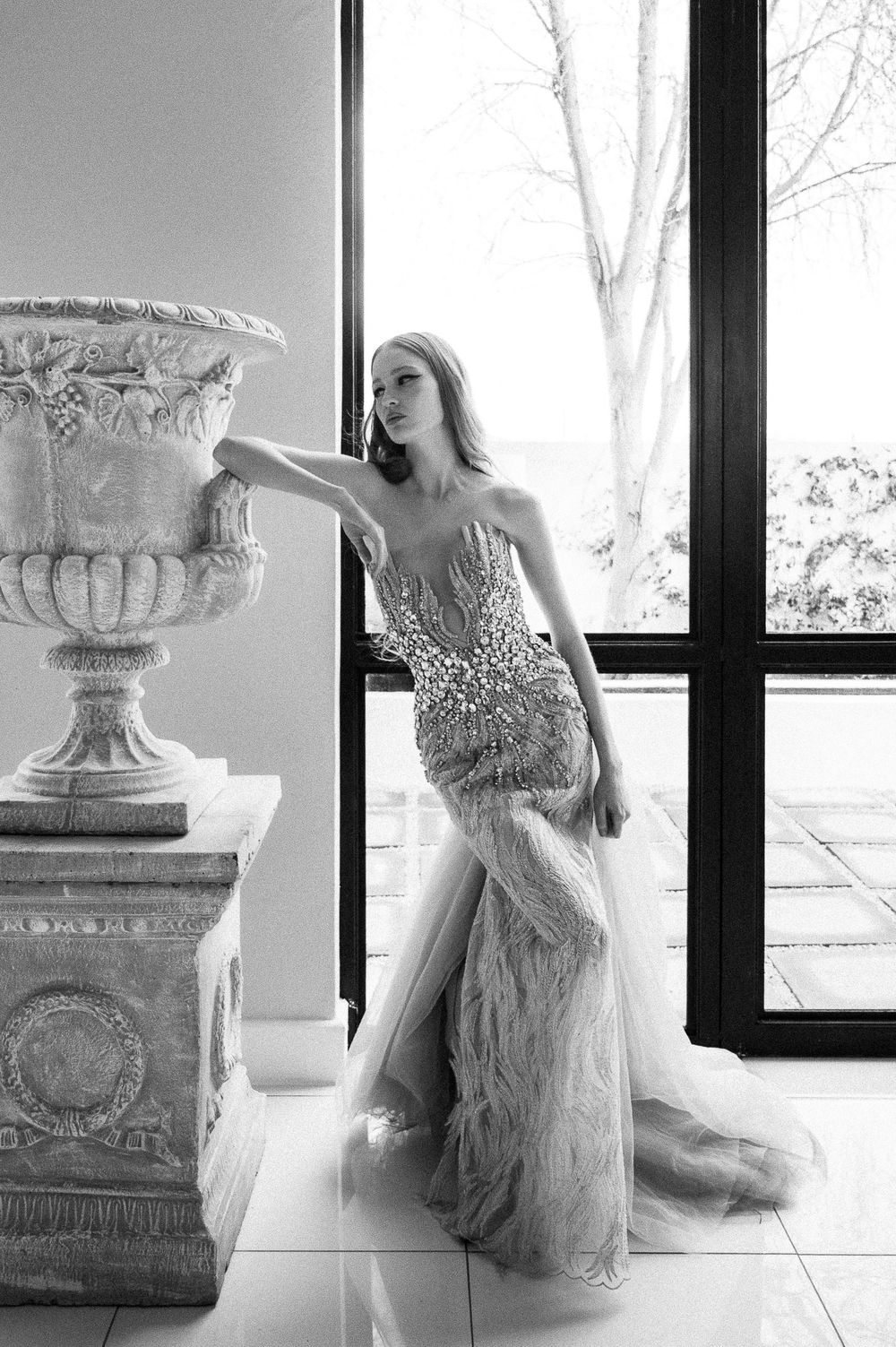 Black and white photo of a dramatic beaded gown with feathers next to classical stone urn.