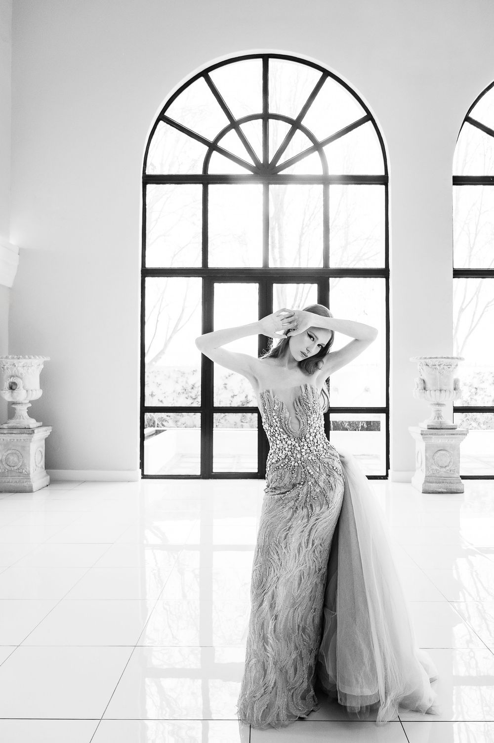 Modern white bridal studio interior with arched windows showing a flowing wedding dress displayed in bright lighting.