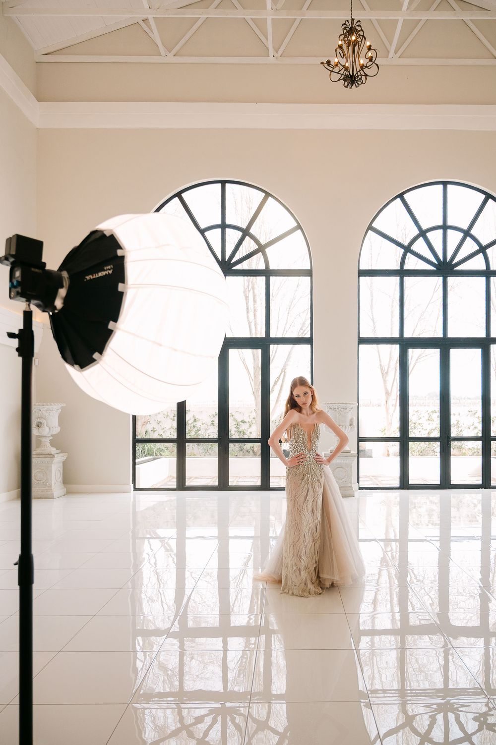 Behind-the-scenes view of a bridal photoshoot with lighting equipment and elegant window backdrops.