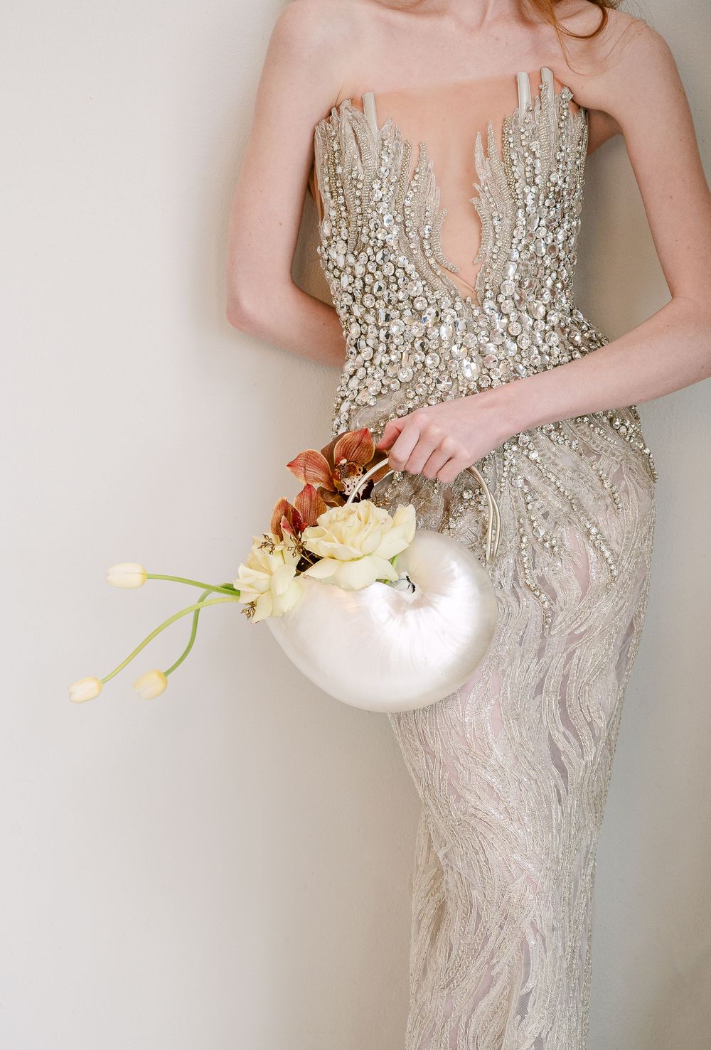 Detail shot of beaded wedding dress and white ceramic vase with delicate flowers.