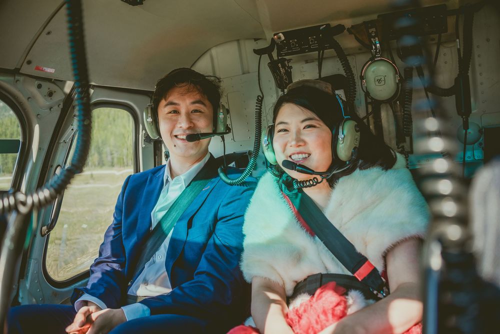 Passengers enjoy a scenic helicopter ride over mountainous terrain with blue skies. Alberta Helicopter Elopement Photographer