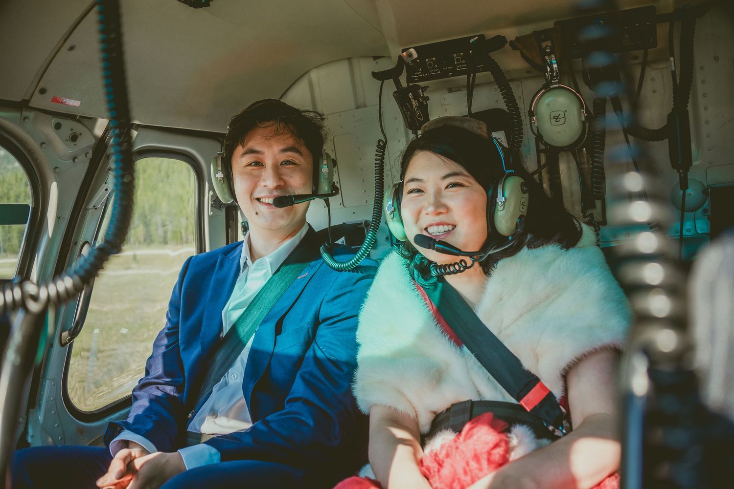 Passengers enjoy a scenic helicopter ride over mountainous terrain with blue skies. Alberta Helicopter Elopement Photographer