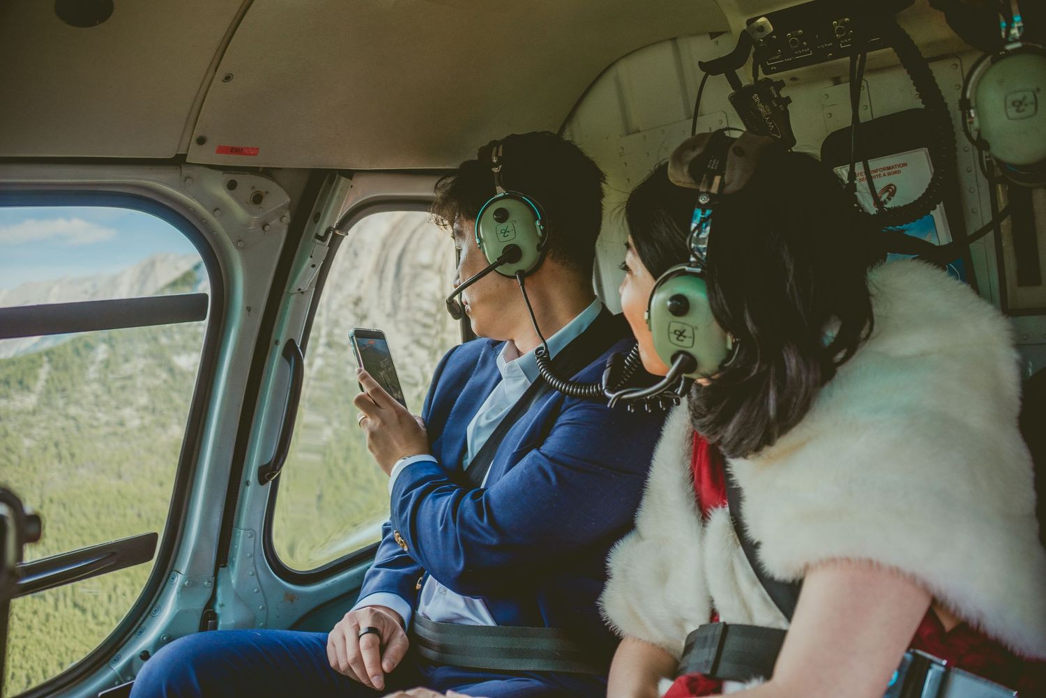Inside a helicopter, passengers with headphones look out the window during a scenic flight. Alberta Helicopter Elopement Photographer